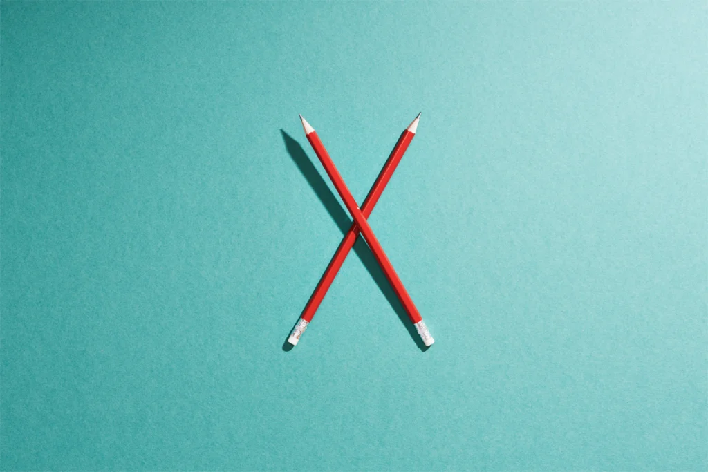 Two red pencils form a letter X against a surf green background.
