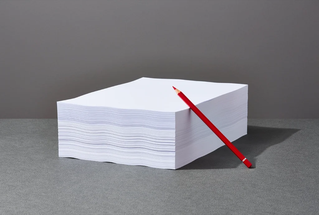 Red pencil leans on a stack of white paper
