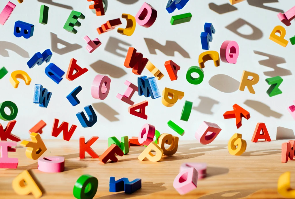 Conceptual image of colorful falling letters, casting shadows on a white wall.