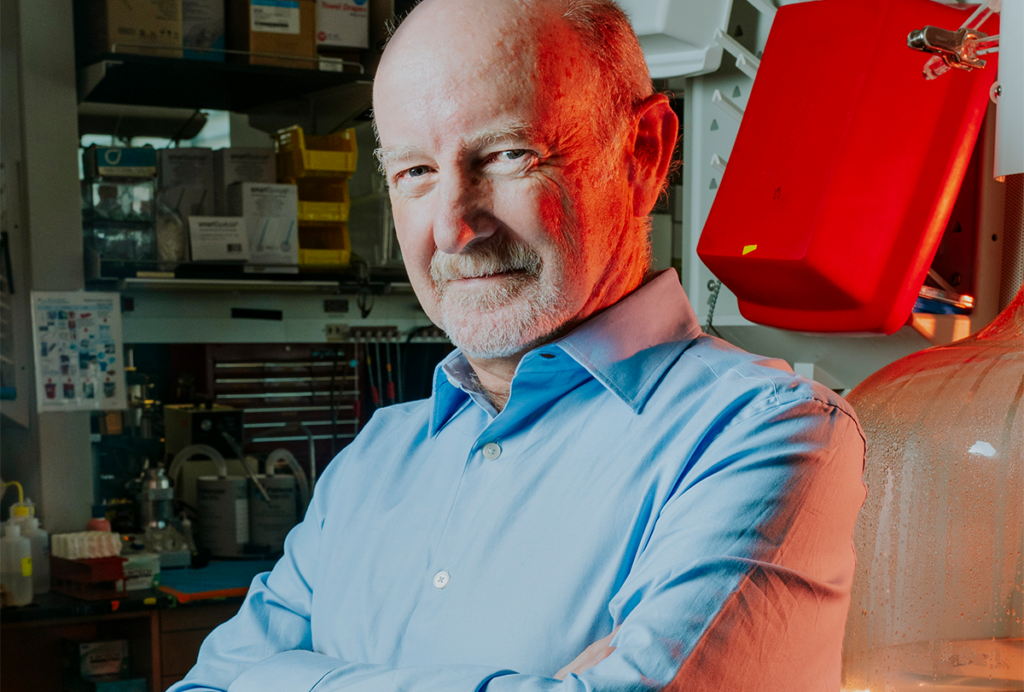 Raphael Yuste leaning on a bench in his lab. A red filter colors the scene.