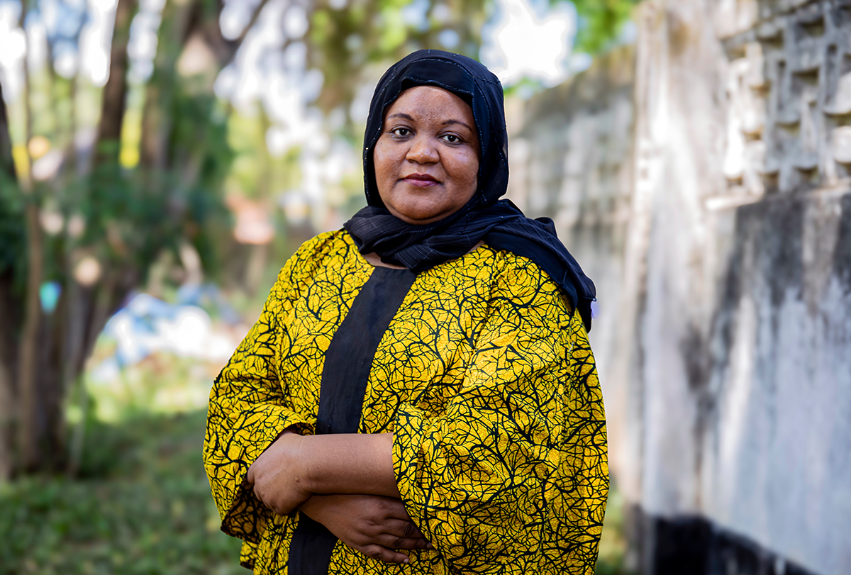 Amina Abubakar, dressed in yellow, stands outside and looks into the camera lens.