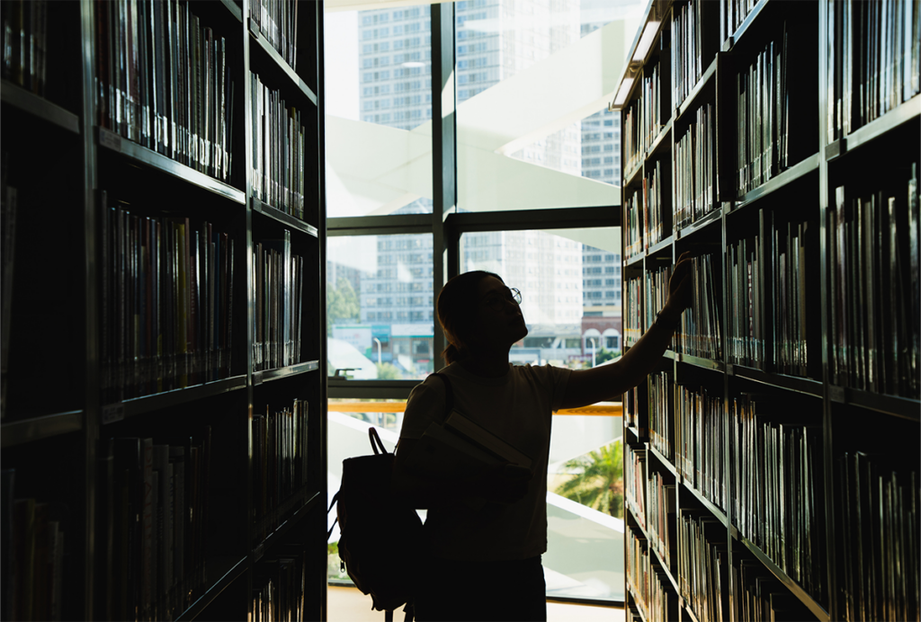 Silhouette of a student in the stacks of a library.