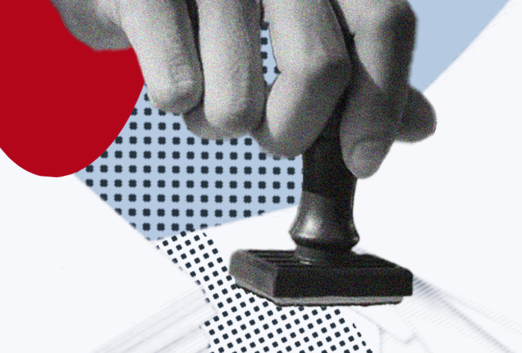 Hand holding a rubber stamp above a stack of papers.