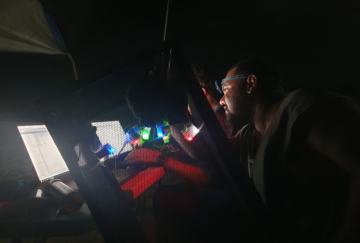 Researchers working on computers at a table set up on a beach at night.