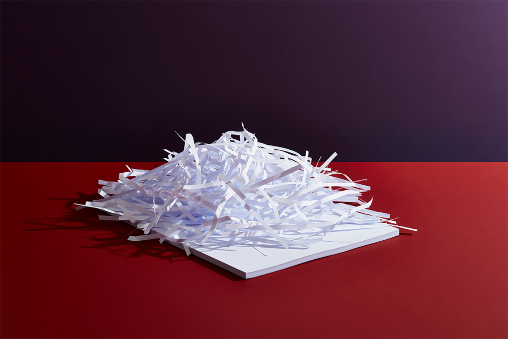 A stack of papers topped by many paper shreddings against a red background.