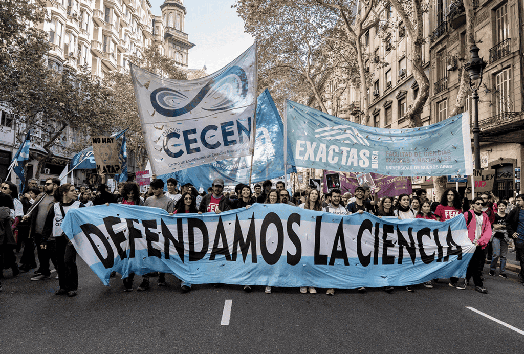 Manifestantes marcham pela rua carregando uma faixa com os dizeres "defendamos la ciencia".