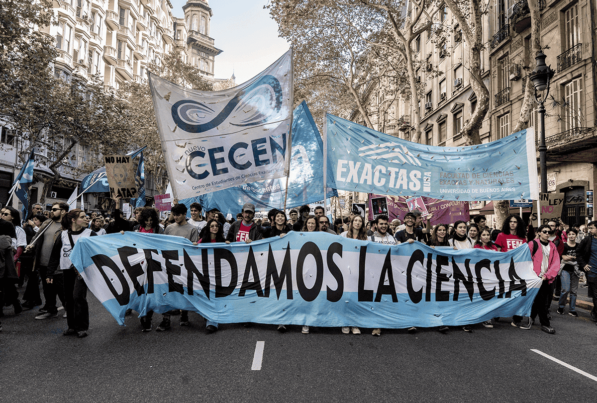 Manifestantes marcham pela rua carregando uma faixa com os dizeres "defendamos la ciencia".