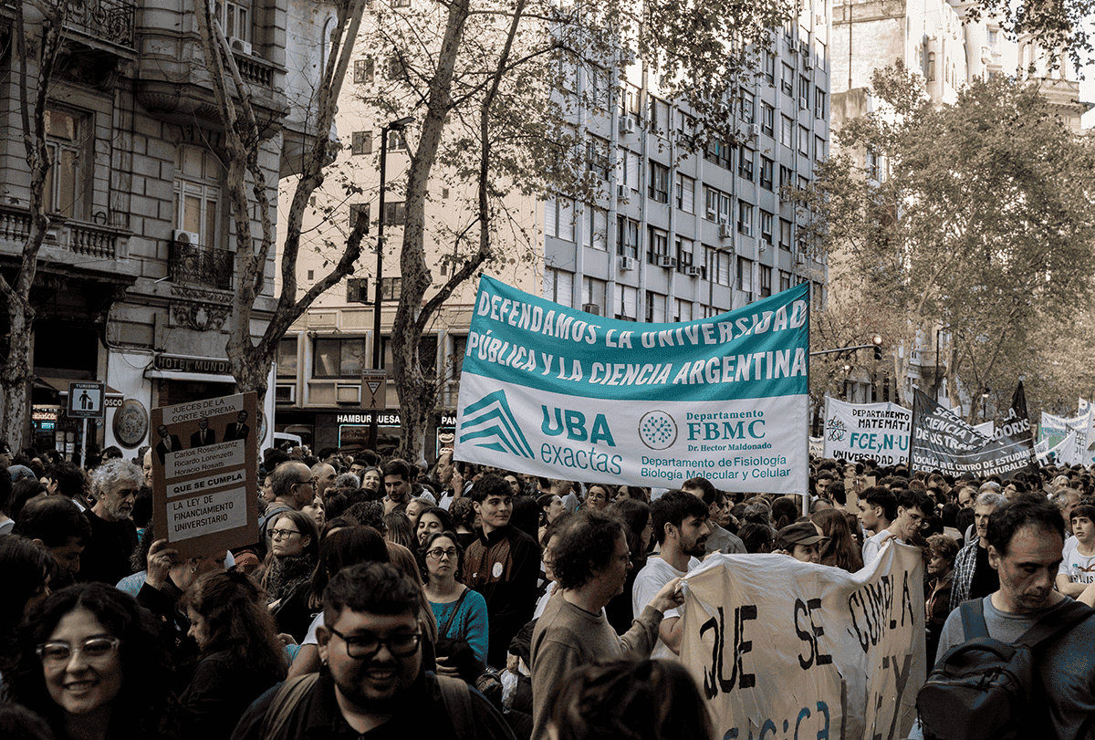 Manifestantes carregam cartazes e entoam palavras de ordem nas ruas de Buenos Aires: uma multidão portando grandes cartazes ocupa as ruas; prédios são visíveis de um lado.