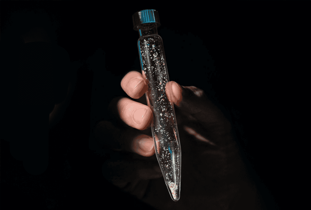 Hand holding a vial of microplastics.