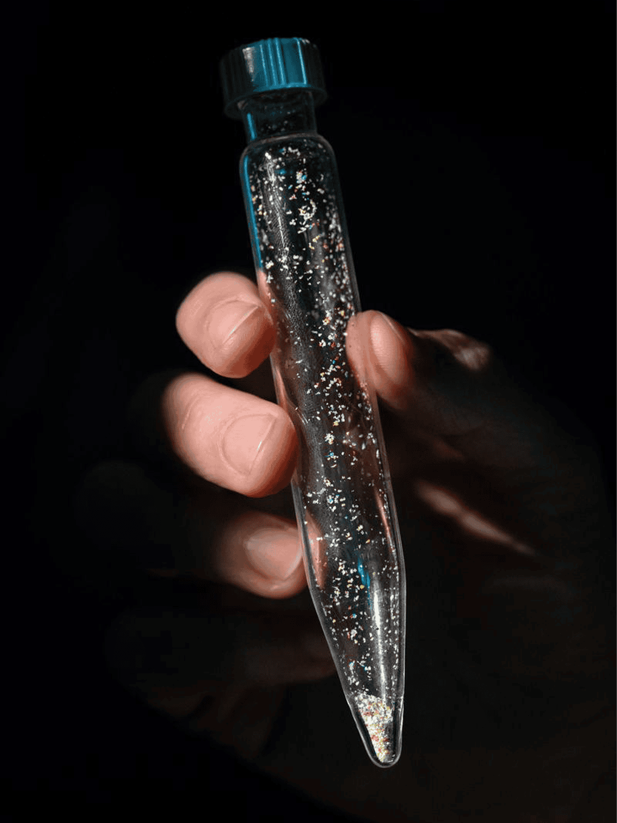 Hand holding a vial of microplastics.