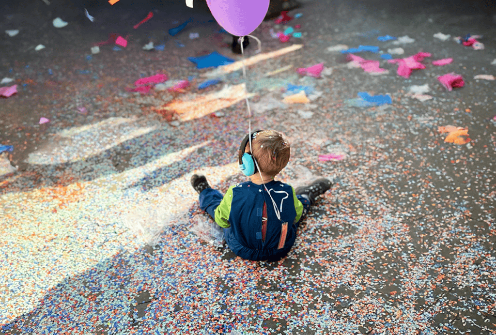 Child sitting on confetti-covered ground, wearing noise-cancelling headphones.