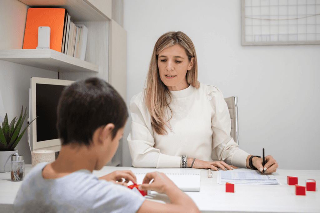 A boy manipulates blocks at a table while sitting across from a woman taking notes.