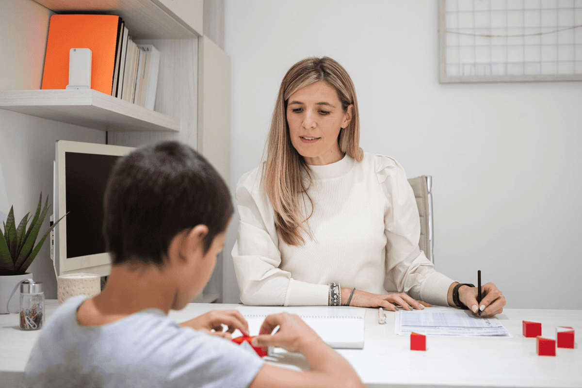 A boy manipulates blocks at a table while sitting across from a woman taking notes.