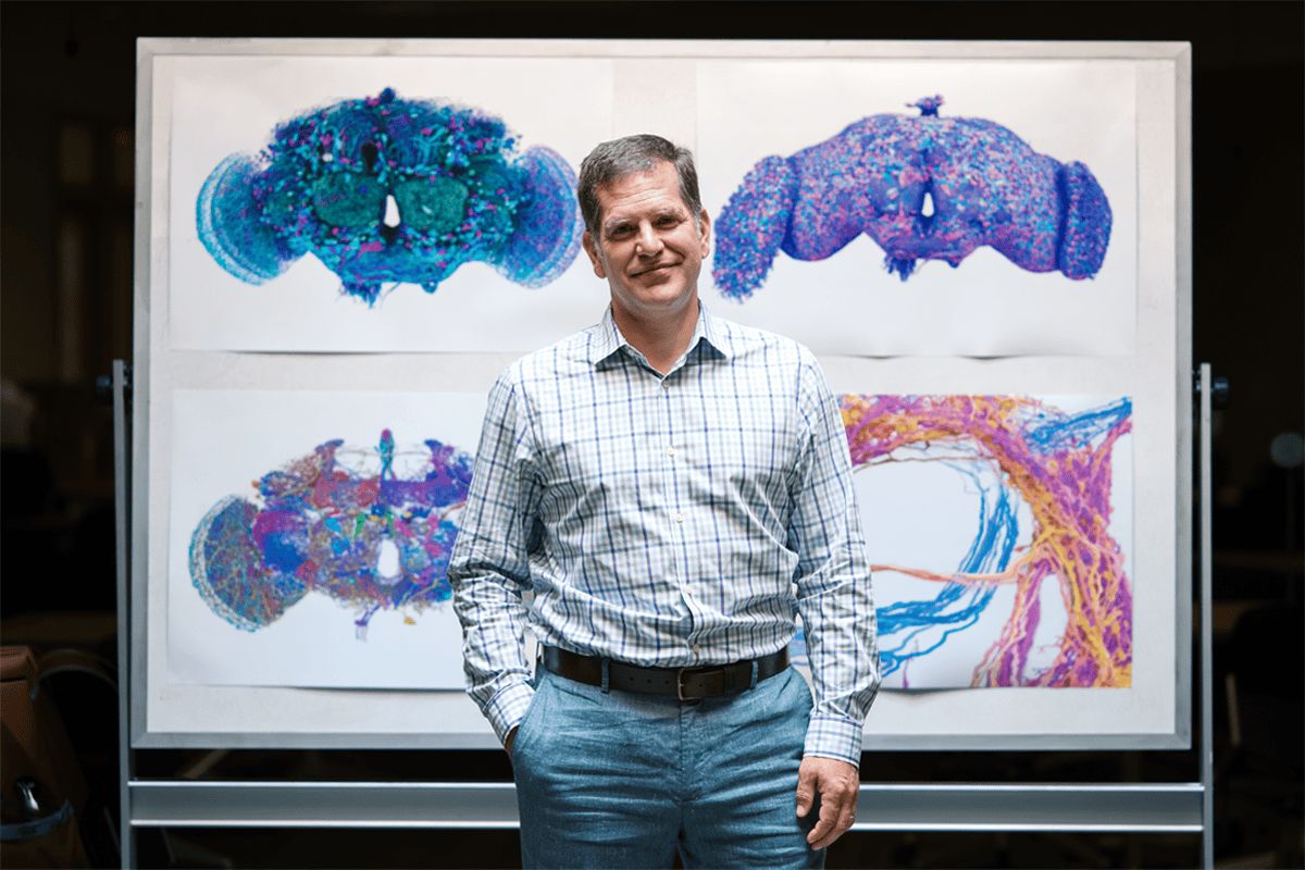 Davi Bock standing in front of a poster showing visualizations of connectomes.